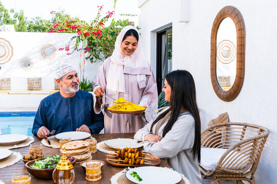 Arab family wearing traditional emirati clothing having lunch at home in the backyard garden - Middle-eastern family bonding and having fun on a family reunion dinner