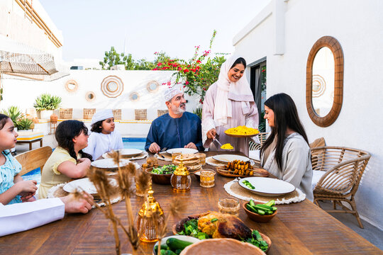 Arab family wearing traditional emirati clothing having lunch at home in the backyard garden - Middle-eastern family bonding and having fun on a family reunion dinner