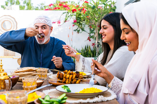 Arab family wearing traditional emirati clothing having lunch at home in the backyard garden - Middle-eastern family bonding and having fun on a family reunion dinner