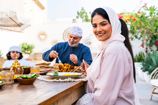 Arab family wearing traditional emirati clothing having lunch at home in the backyard garden - Middle-eastern family bonding and having fun on a family reunion dinner