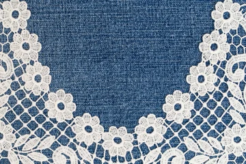 Lace trim on denim fabric shows detailed patterns and textures in a close-up view during daylight hours © Fleuronica