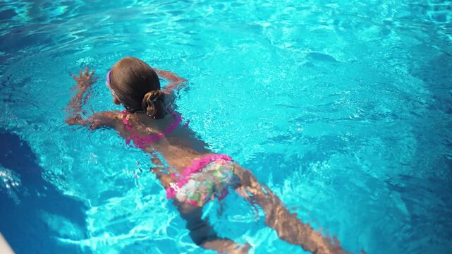 A girl in a pink bathing suit in purple glasses floats on a pool with blue water on a summer day