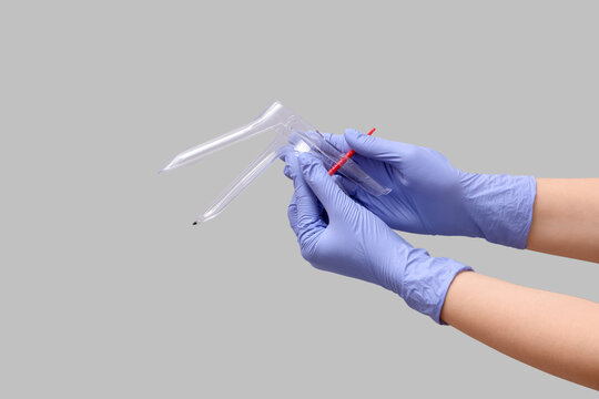 Doctor's hands with gynecological speculum on grey background