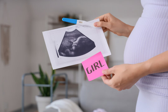 Pregnant woman with sonogram image,  pregnancy test and paper with word GIRL in living room. Closeup
