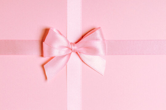 Pink satin ribbon bow centered on pink background close-up