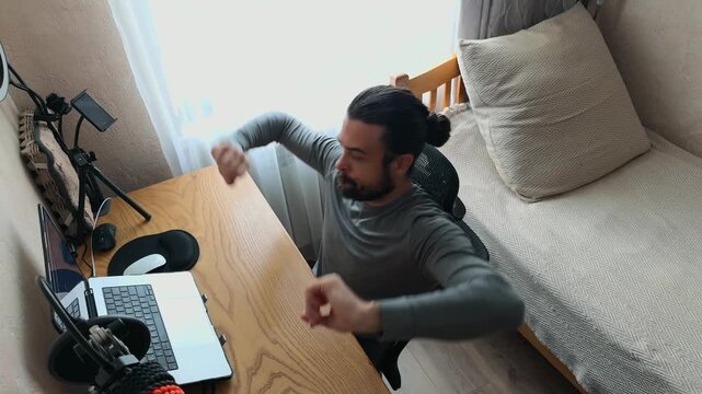 Caucasian Young Male Professional with Man Bun Tired Working on Laptop Stretching Arms Yawning at Desk Leaning Back and Cracking Knuckles Finishing Day Standing up and Walking Out of Home Office Shot