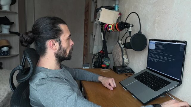 Recognizable Caucasian Young Man with Man Bun Hair Typing on Laptop then Shutting Down Closing Lid Standing Up and Finishing Work in Cozy Home Office Bedroom Interior Side View Profile daylight shot