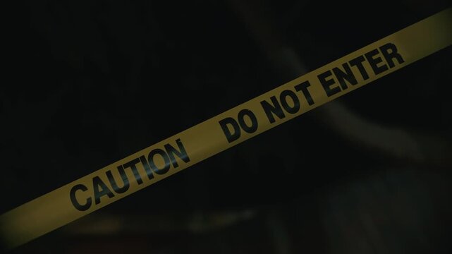 Yellow caution tape do not enter blocking dangerous zone at night indicating restricted access and perimeter control in dark outdoor environment