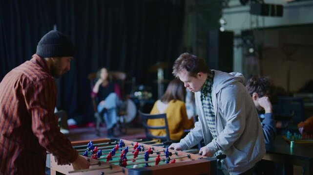 A young man with Down syndrome plays foosball with a friend. They enjoy a fun and inclusive game together in a casual environment.