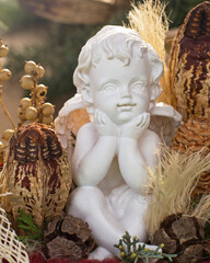 Obraz premium Small statue of a cherub sits among pine cones and dried plants in a decorative setting during the day