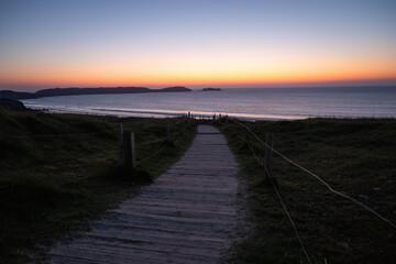 Fototapeta premium wooden boardwalk leading to ocean beach at sunset with colorful sky and calm sea horizon