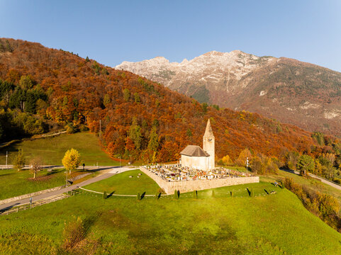 Vibrant autumn landscape with historic San Tommaso church on a green hill, surrounded by colorful foliage and majestic mountains, a prime tourism destination in Cavedago, Paganella, Trentino, Italy.