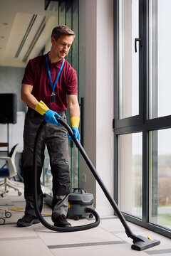 Smiling commercial cleaning worker vacuuming office building floors.