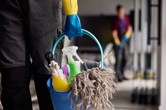 Close up of housekeeping worker carrying bucket filled with cleaning products.
