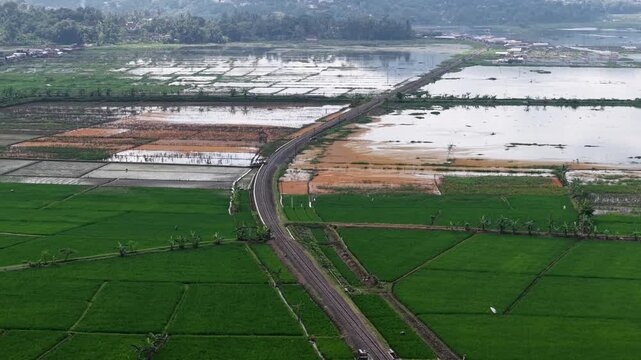 An aerial view of the still-functioning Dutch colonial railway crossing Lake Rawa Pening. The nostalgic tourist train route uses diesel locomotives and classic wooden carriages.