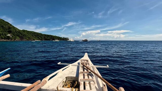 Sailing POV in an outrigger boat in the wavy blue sea with the view of distant island and moored boats at the horizon. Summer travel vacation in Dauin, Philippines