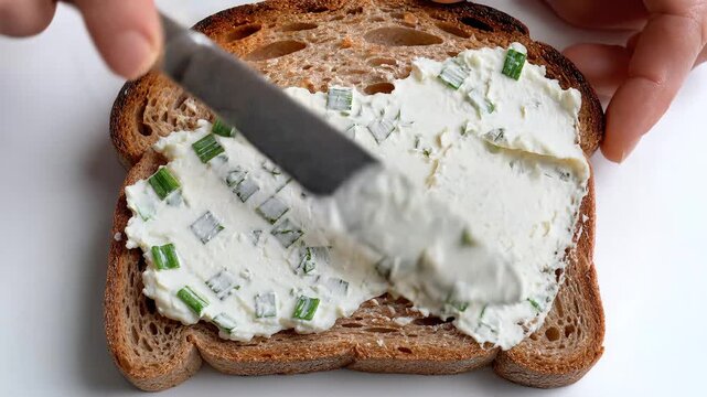 Spreading cream cheese with fresh chives on toasted sourdough bread close up on white background