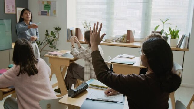 Medium arc shot of Hispanic female teacher explaining stages of pregnancy at lesson in high school, shy confused African American schoolgirl raising hand and asking question while classmates watch