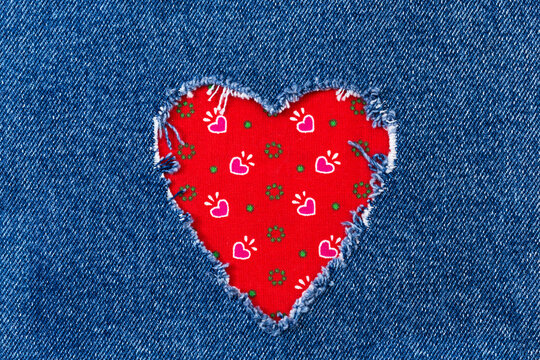 Denim fabric with a heart-shaped hole revealing red patterned fabric underneath in a close-up view