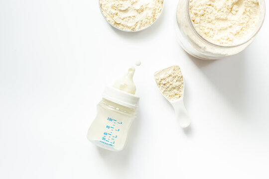 Baby milk bottle and powdered infant formula in the jar and scoop on white background. Top view.