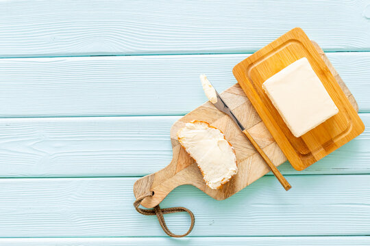 Block of butter in wooden butter dish and a knife with crispy toast with butter on cutting board, top view
