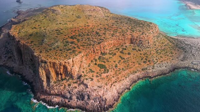 Cinematic aerial of Gramvousa island with vibrant ochre cliffs and emerald turquoise water. Close up revealing second island in Balos bay, Crete. Mediterranean nature and exotic sea colors, 4k.