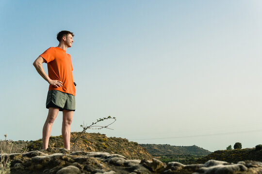 Young runner standing on hill looking ahead at landscape