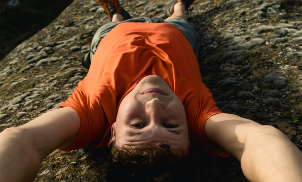 Man smiling taking selfie while lying on rocks