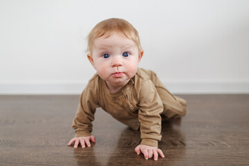 Naklejka premium Portrait of an infant in a brown outfit propped up on hands on a dark floor