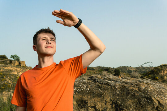 Young man sheltering eyes from sun exploring nature