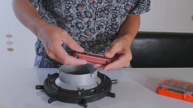 Person tightening bolts on softbox light mount using multitool, assembling studio lighting equipment at home or workshop, setup process for photography or video production, close up of hands