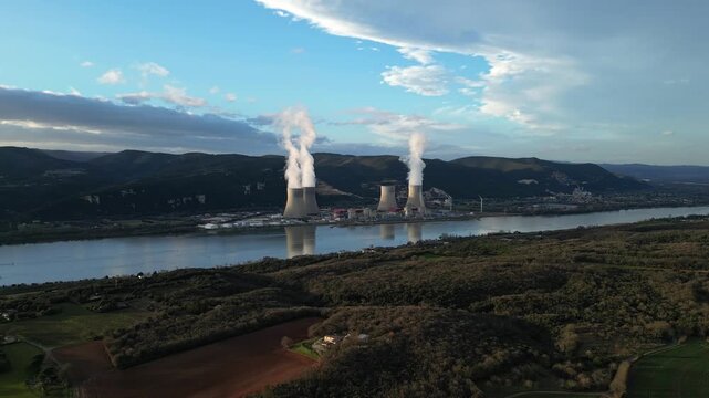 Cruas, France - 20 February 2026: Aerial drone view of the Cruas nuclear power plant in France, with cooling towers producing steam beside the Rh&ocirc;ne River during a dramatic sunny afternoon landscape.
