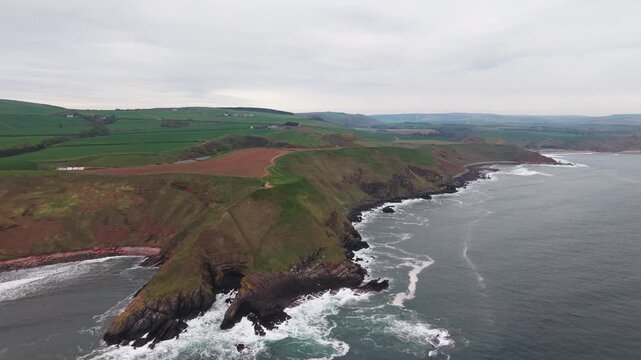 Dramatic aerial approach to a rugged rocky cape and high cliffs on the Scottish coastline.