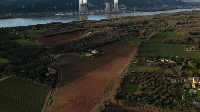Cruas, France - 20 February 2026: Aerial drone view of the Cruas nuclear power plant in France, with cooling towers producing steam beside the Rh&ocirc;ne River during a dramatic sunny afternoon landscape.