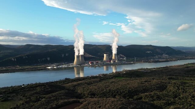 Cruas, France - 20 February 2026: Aerial drone view of the Cruas nuclear power plant in France, with cooling towers producing steam beside the Rh&ocirc;ne River during a dramatic sunny afternoon landscape.