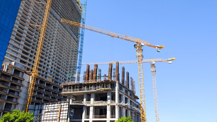 Building cranes constructing a new modern skyscraper and developing urban infrastructure under a clear blue sky, illustrating growth and ongoing construction work © Newleks