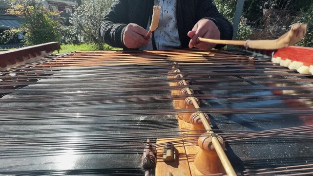 Street performer play traditional cymbal musical instrument with sticks over strings, slow motion