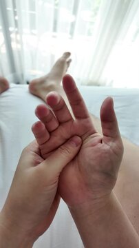 Man massaging his palm and fingers on a white bed to relieve pain and stiffness. Self-care, trigger finger, and office syndrome recovery concept. 4K vertical resolution