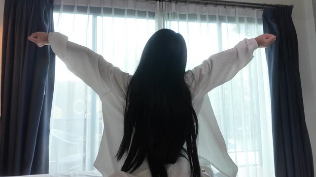 Slow motion of rear view of young woman wearing white pajamas, sitting on a bed and stretching relaxing in the morning. Concept of relaxation and healthy routine. 4K horizontal resolution