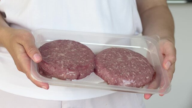 Closeup raw burger patties in packaging held by woman hands, ideal for grocery and cooking content. Beef emphasizes product quality and meal preparation. 