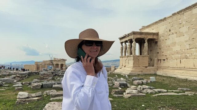 Archeologist woman with hat talk to  phone at Acropolis in Athens looking at Caryatid Porch on ancient Erechtheion or Erechtheum temple