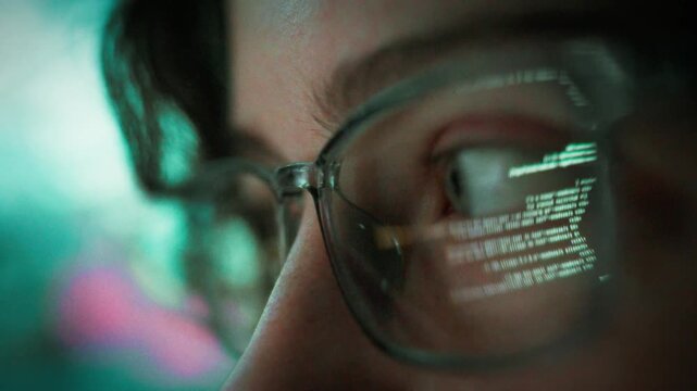 At night a young programmer sits before a glowing PC monitor, typing code while the screen's light reflects in her glasses, highlighting the focused atmosphere of a modern coding session