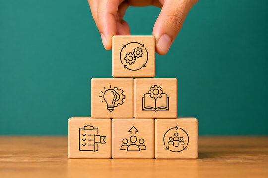 Hand stacking a wooden block with circular gear symbols over various business team management checklist and innovation icons on a desk against a green background