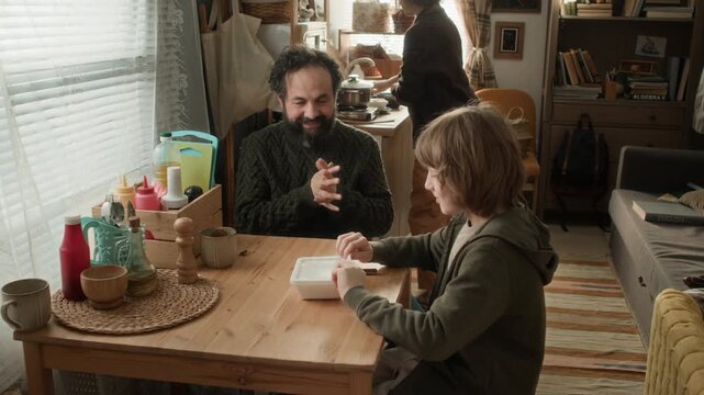 High angle shot of mother serving instant noodles to her husband and son, sitting at table in poor, cramped apartment