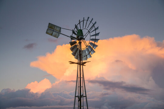 Farm windmill silhouetted against a pink thunderhead over rural farmland