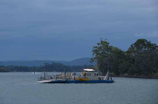 Vehicle ferry crossing river in sun, clouds and trees in background