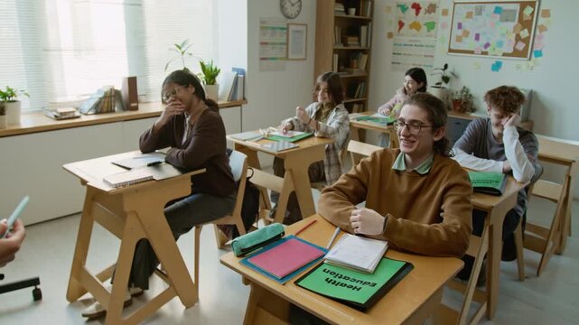 Medium pan shot of female teacher discussing birth control methods with class of laughing diverse teenage students, nerdy Caucasian boy in glasses expressing opinion on responsible pregnancy planning