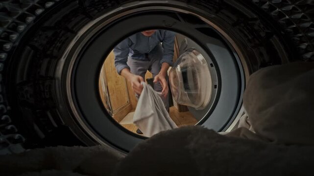 A man loads soiled garments into a laundromat's washing machine, adding detergent, and initiates the cleaning cycle, efficiently managing dirty laundry in the laundry room