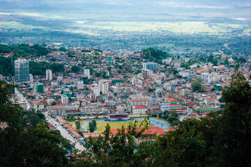 Fototapeta premium Scenic overview of a mountain city surrounded by forests and valleys, showing dense urban development blending with the natural landscape in Southeast Asia.