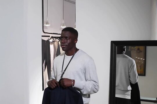 Thoughtful customer holding garments while deciding purchase inside contemporary minimalist clothing boutique